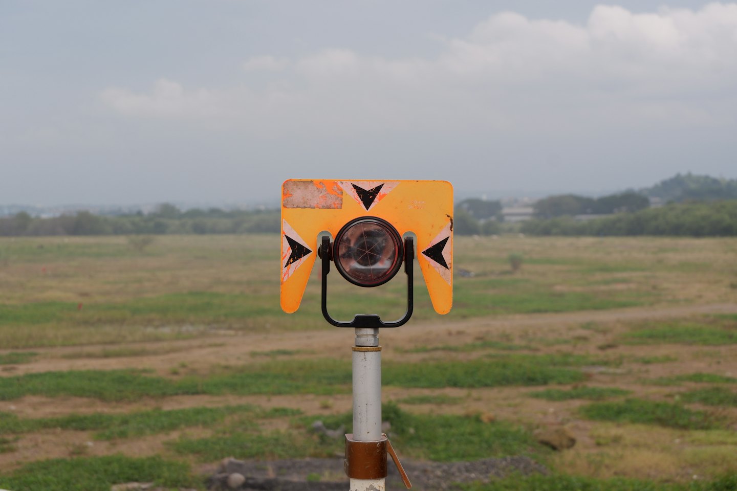 Orange surveying prism mounted on a pole in a field.